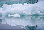 The backdrop of this fine-art photograph is formed and filled by a bigger iceberg with reflection in the water. Smaller elegantly shaped pieces of ice are passing in the foreground. Different shades of ice-blue color tones and cracks in the ice create a symmetric and well-balanced image that almost feels abstract. Picture was taken at the Sermilik fjord in East-Greenland.