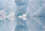 The backdrop of this fine-art photograph is formed and filled by a bigger iceberg with reflection in the water. Smaller elegantly shaped pieces of ice are passing in the foreground. Different shades of ice-blue color tones and cracks in the ice create a symmetric and well-balanced image that almost feels abstract. Picture was taken at the Sermilik fjord in East-Greenland.