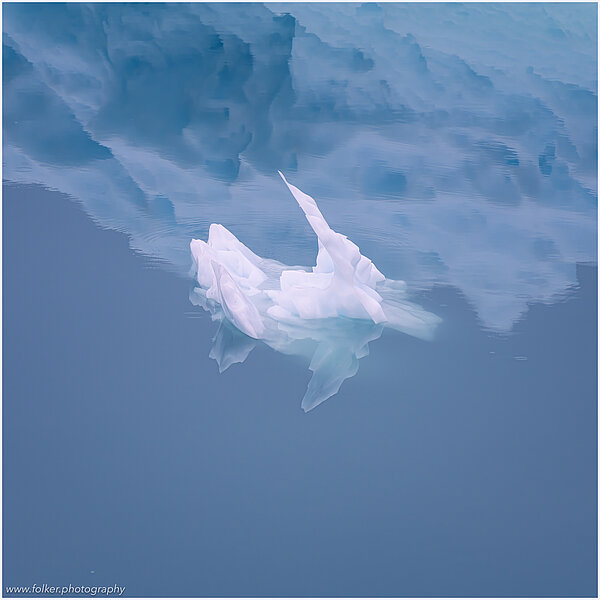 This fine-art photograph shows a minimalistic detail of a small iceberg in front of the reflection of a bigger iceberg. Picture was taken at the Sermilik fjord in East-Greenland. 