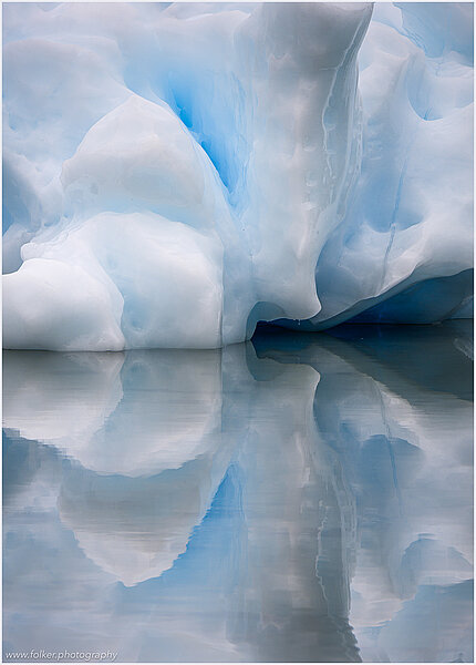 This fine-art photograph shows a minimalistic detail of an iceberg with reflection in the water. Nature created a beautiful abstract with cracks and layer of ice colors. Picture was taken at the Sermilik fjord in East-Greenland.
