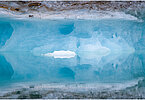 The backdrop of this fine-art photograph is formed and filled by a bigger iceberg with reflection in the water. Smaller elegantly shaped pieces of ice are passing in the foreground. Different shades of ice-blue color tones and cracks in the ice create a symmetric and well-balanced image that almost feels abstract. Picture was taken at the Sermilik fjord in East-Greenland.