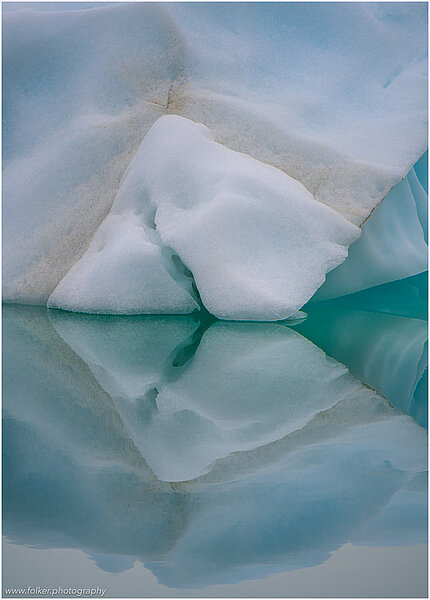 This fine-art photograph shows a minimalistic detail of an iceberg with reflection in the water. Nature created a beautiful abstract with cracks and layer of ice colors. Picture was taken at the Sermilik fjord in East-Greenland.