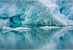The backdrop of this fine-art photograph is formed and filled by a bigger iceberg with reflection in the water. Smaller elegantly shaped pieces of ice are passing in the foreground. Different shades of ice-blue and green color tones and cracks in the ice create a symmetric and well-balanced image that almost feels abstract. Picture was taken at the Sermilik fjord in East-Greenland.