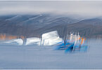 This fine-art photograph shows an abstract, painterly scene in Tassilaq in East-Greenland. In a style of a painting from early 20th century, you can imagine to see an iceberg and a blue ferry in front of cloudy mountains.